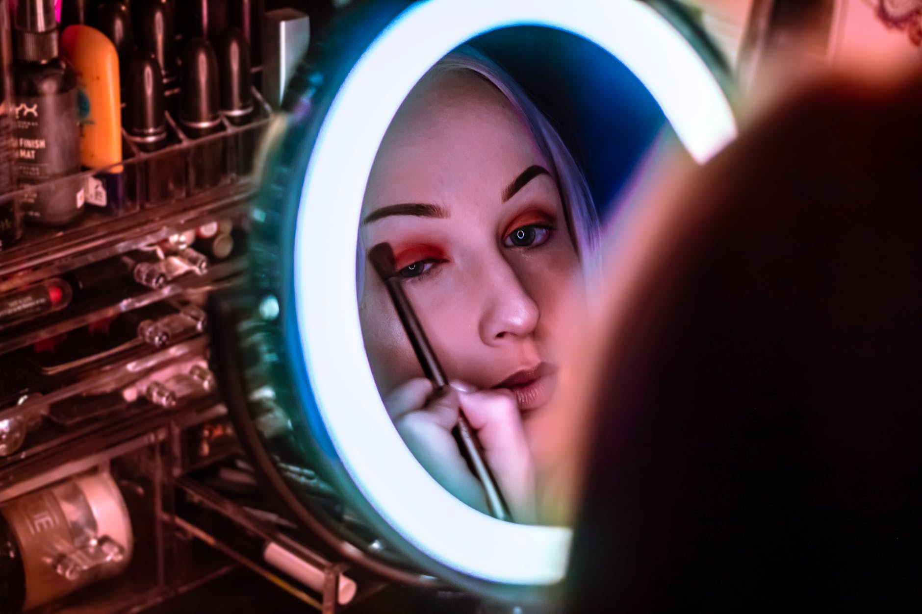 woman facing mirror applying eyeshadow